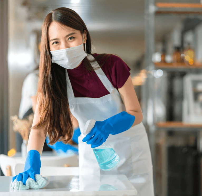 Spotless Solutions staff wiping a counter surface with a mask and cleaning gear